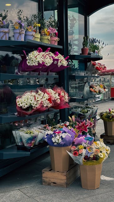 A display of various floral arrangements at flowerdeliveryfulham.co.uk, featuring colorful bouquets of fresh flowers arranged on a multi-tiered black shelf inside a glass-enclosed space. The arrangeme