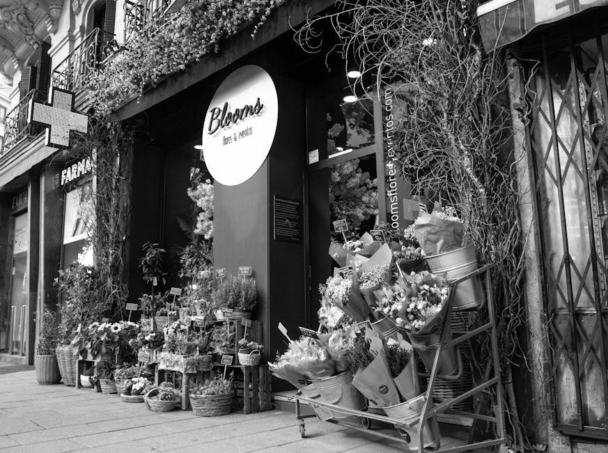 A floral shop storefront decorated with an array of fresh flower bouquets and arrangements arranged in wicker baskets, paper wraps, and metal buckets placed on wooden crates and on a rolling cart outs