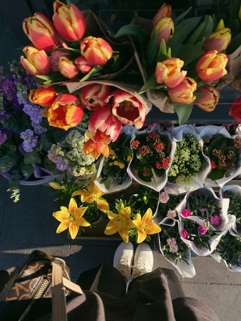 A vibrant display of fresh flowers from flowerdeliveryfulham.co.uk arranged in a variety of bouquets. Prominently, there are orange and yellow tulips with streaks of red on their petals, positioned in